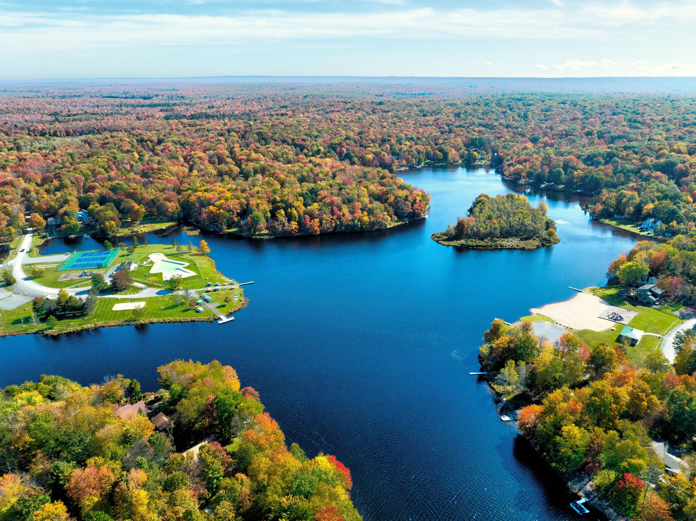 Wide aerial view of a Poconos lake in fall color, near a lakefront home at Arrowhead Lake